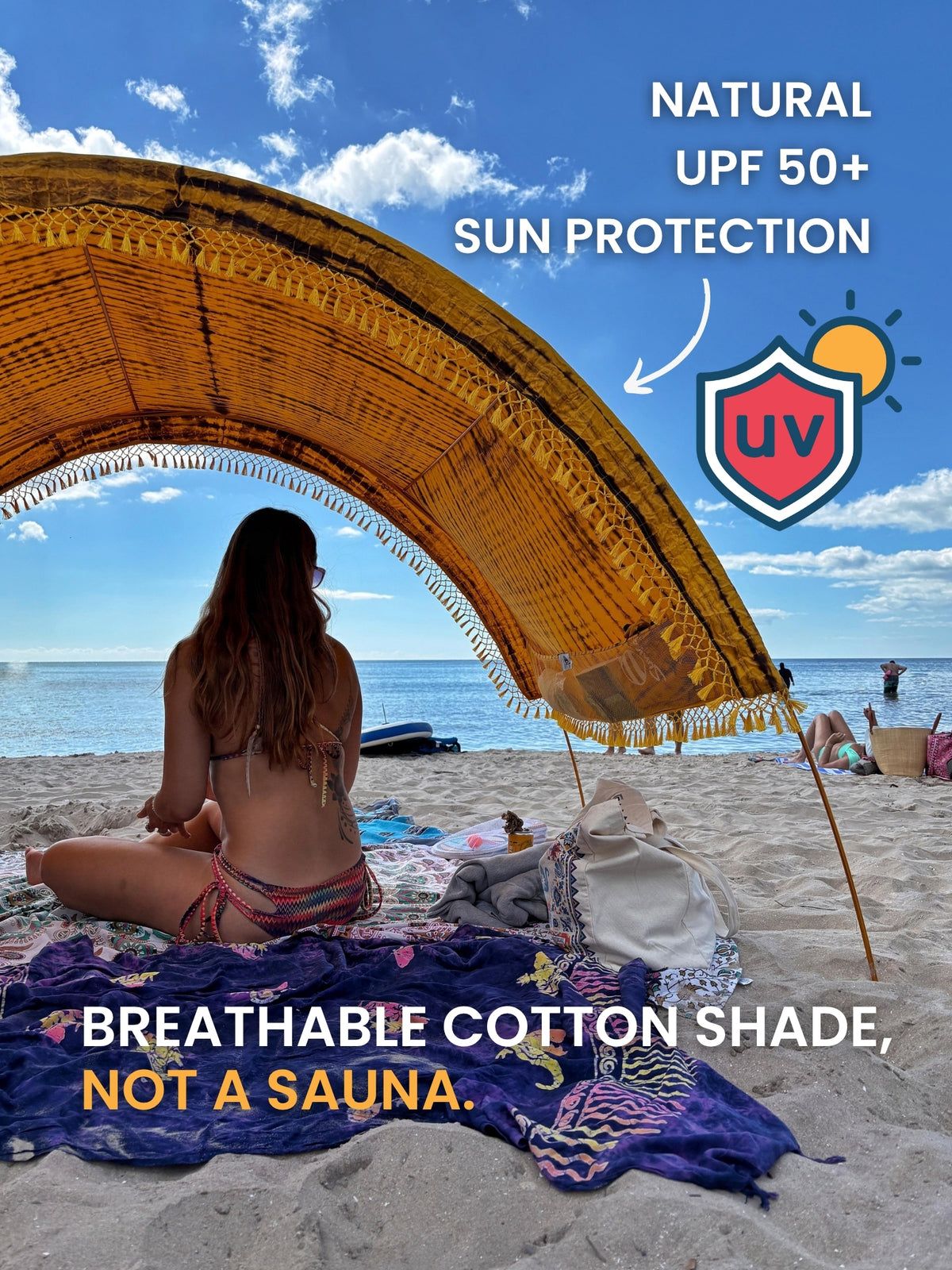 Woman sitting under a Tiger’s Eye tie-dye Suniela beach cabana looking at the ocean, breathable cotton shade with UPF 50+ sun protection