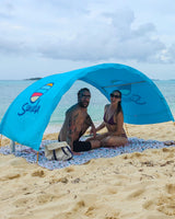 Couple sitting beneath an arched, blue Suniela shade cabana on a sandy beach