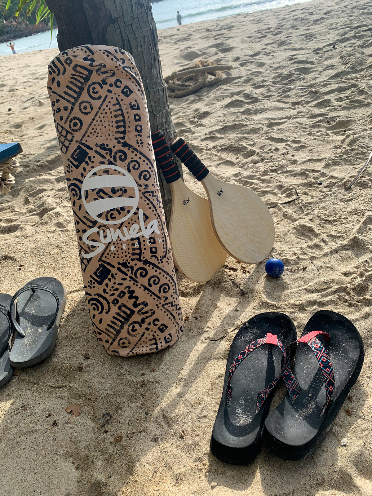 A  beach scene with flip flops and a Tan coloured Suniela Beach shade cabana next to a paddleball game