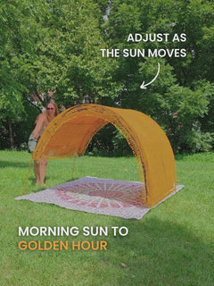 Video of a woman sliding the adjustable canopy of a Tiger’s Eye Suniela portable beach cabana from side to side on park grass, so the shade follows the sun.