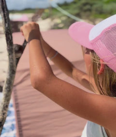 two kids play in and around the shade of their beige coloured cotton cabana  tent on a sandy beach with tropical foliage in the background