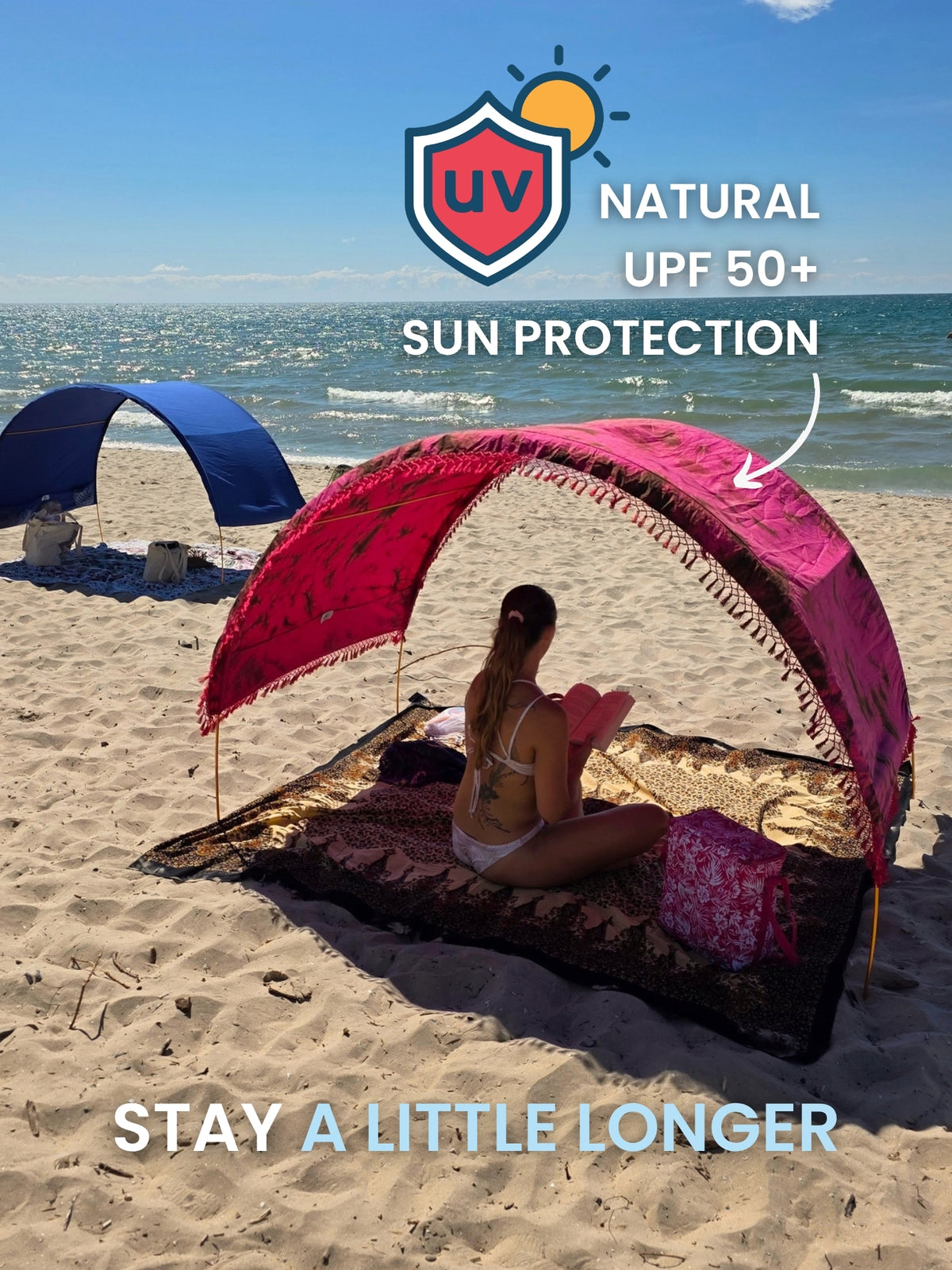 Woman reading a book under a Hibiscus Bloom Suniela portable beach cabana on the beach, with hand-dyed cotton shade giving natural UPF 50+ sun protection.