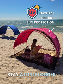 Woman reading a book under a Hibiscus Bloom Suniela portable beach cabana on the beach, with hand-dyed cotton shade giving natural UPF 50+ sun protection.